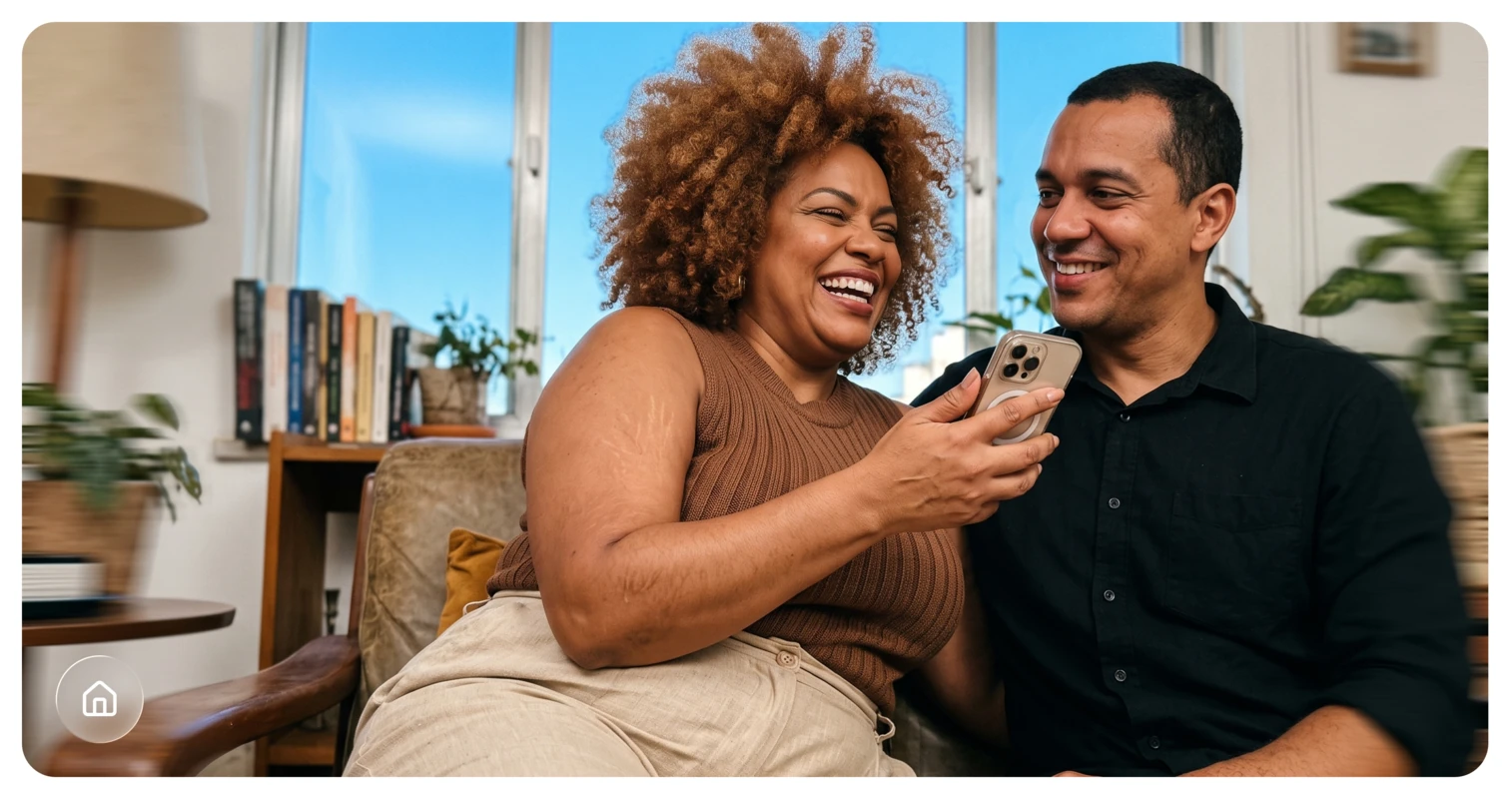 Casal sorrindo em casa, olhando para um celular